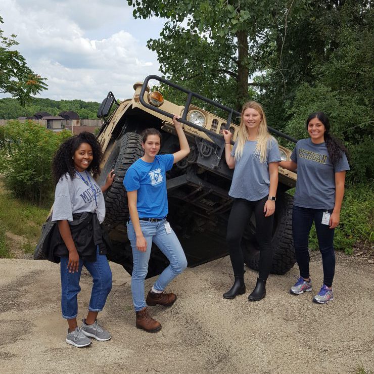 AM General Interns posing in front of a humvee that is climbing a steep hill at the Mishawaka Training course